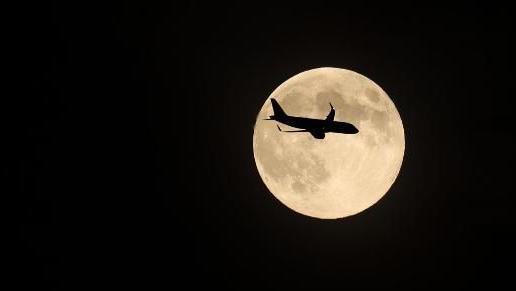 A silhouette of a plane crossing the supermoon.