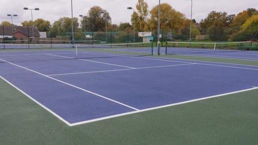 A blue tennis court with nets set up. The surround of the court is green.