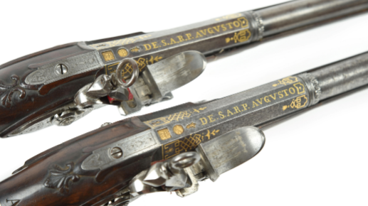Two decorative 18th Century pistols against a white background with the words "DE. S.A.R.P. AUGUSTO" written on them in golden gilt.