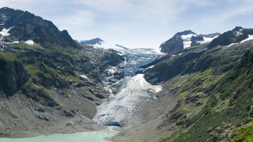 A blue lagoon underneath a white snowy glacier, framed by tall green mountains either side