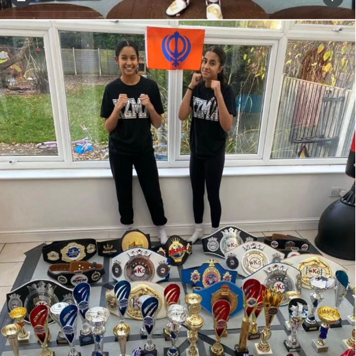 Dheep and Simran dressed all in black stood in front of lots of belts and trophies in a conservatory