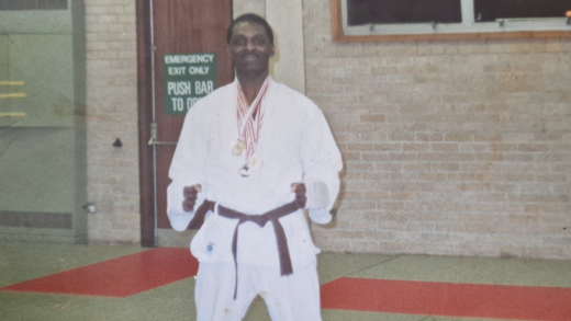 Lloyd Russell in his karate uniform. He has medals around his neck and is raising his fists.