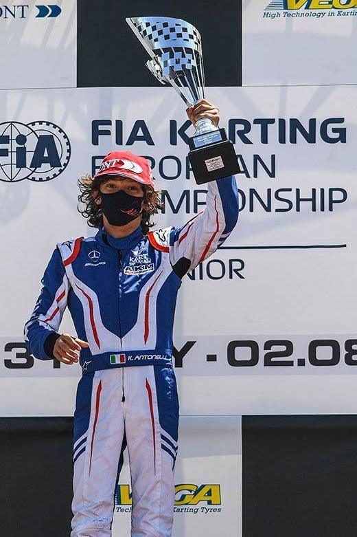Kimi Antonelli, who is wearing a mask, holds aloft a trophy on the podium after the European Karting Championships in 2021