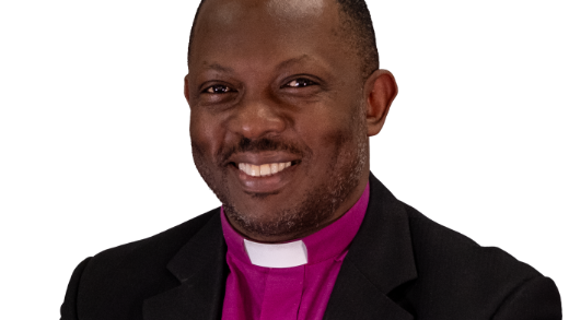 Head and shoulder shot of Bishop Wambunya wearing a purple cassock, white collar and black jacket. 