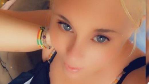 A selfie of a woman with blonde hair and blue eyes. She is wearing two multicoloured bracelets on her wrist.