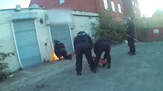 Four police officers in riot gear cut open a metal shutter outside a commercial property.