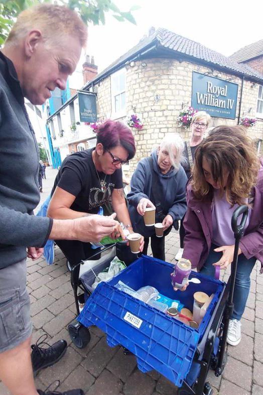 Five volunteers of Let Them Eat Cake taking hot drinks from a trolley to hand out to people in Lincoln in front of Royal William IV pub