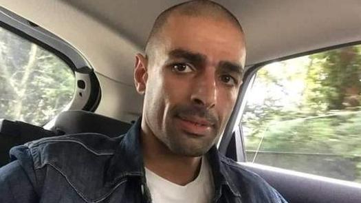 An image of Jermaine Mazlum sitting in what appears to be the back of a moving car, wearing a denim over-shirt.