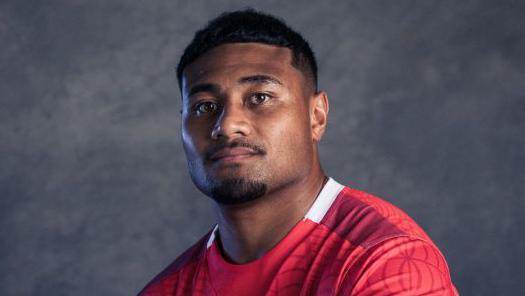 A portrait photo of Sam Moli in a red Tonga rugby jersey.