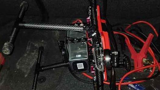 A black drone next to some jump leads in a car's boot