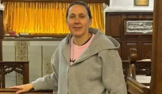 Nikki Dilorenzo standing in a church. She's wearing a grey hoodie and pink jumper