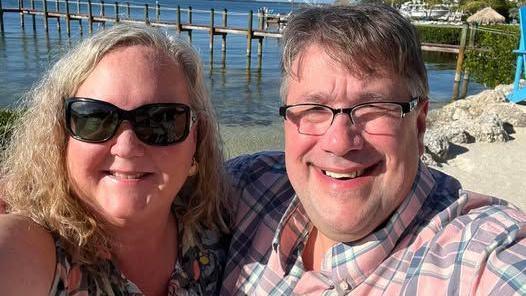 Khraila and Donald Yowell smile for a selfie together outdoors in front of a bridge.