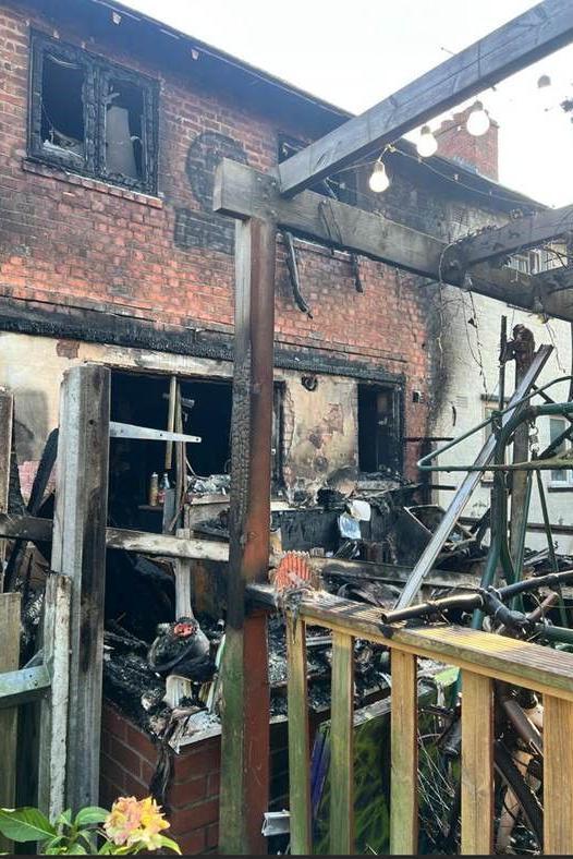 A view of the completely destroyed conservatory at Mr Hettiarachchi's home, including burnt and broken windows and doors, charred wooden beams and bricks, and piles of the remnants of various items