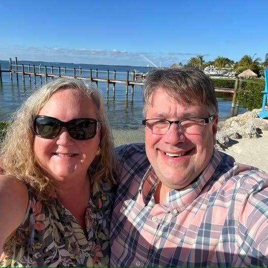 Khraila and Donald Yowell smile for a selfie together outdoors in front of a bridge.