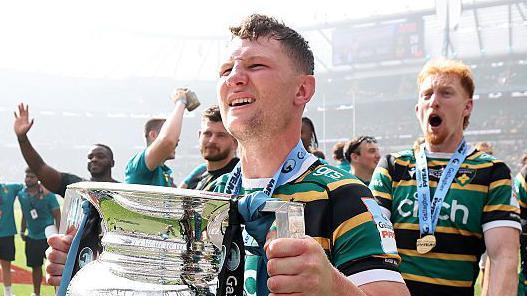 Fraser Dingwall holds the Gallagher Premiership trophy on the pitch at Twickenham as he and other Northampton Saints players celebrate