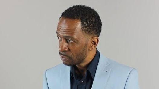 Granville Graham, wearing a light blue suit and navy shirt, in a studio head-and-shoulders photo in which he is looking slightly to the right. He has black hair and styled facial hair.