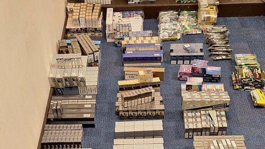 Hundreds more boxes and bags of different tobacco products laid out on a blue office carpet. 