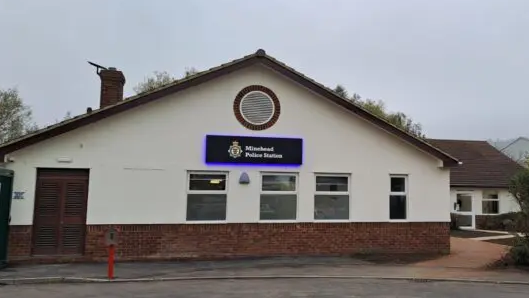 The new Minehead Police station is a white building. It has an illuminated sign on the front, saying Minehead Police Station.