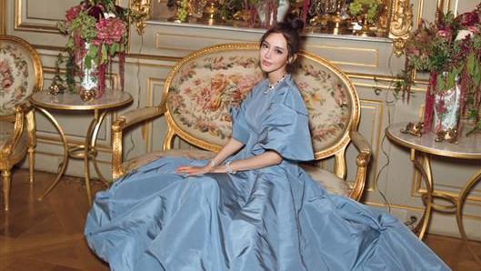 Ms Huang poses on an ornate sofa in a palatial room wearing an enormous blue ballgown