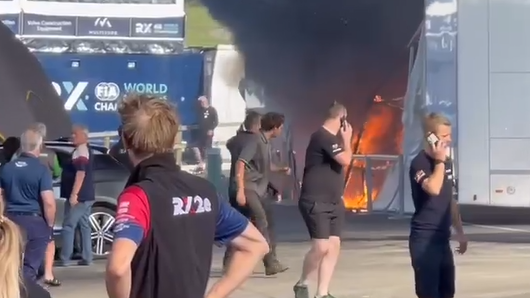 Race trackers look on smoke and flames on a race track