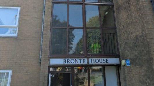 Image shows the entrance to Bronte House. A white band above the door spells out the building's name in dark capital letters. A fire officer in a high visibility jacket can be seen climbing the stairs through the glass panelling above the front door.