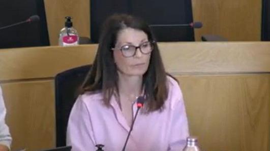 A woman with long dark hair wearing a pink shirt