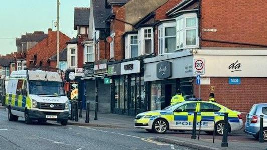 A police van and a police car on a street with shops.