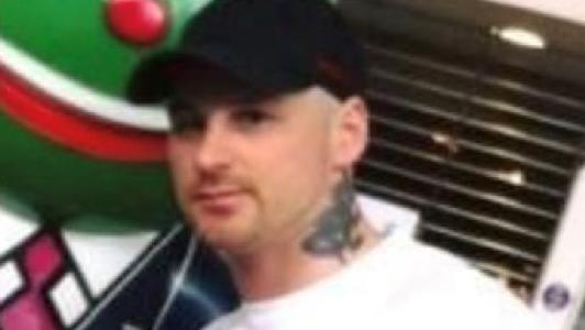 A man with a prominent neck tattoo wearing a black cap and white tshirt.