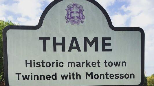 A white road sign with black writing which reads: Thame, historic market town, twinned with Montesson