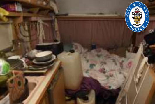 The living conditions inside the caravan. Dishes are piled up on the side and a duvet and containers are situated in the middle 