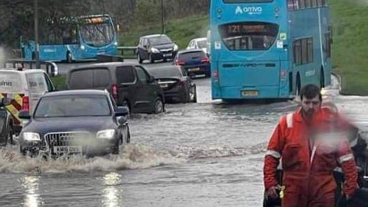 The picture shows vehicles driving through flooded roads with two buses and several cars visible.