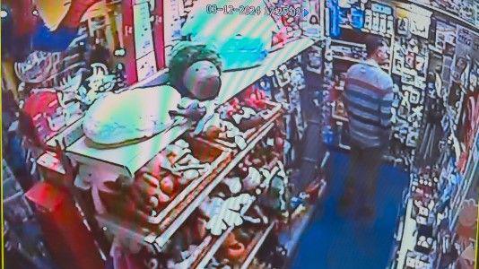 A colourful CCTV image inside the toy shop. Mr Nairn is wearing a stripey jumper and has his back to the camera. There are shelves of toys all around him. The shoplifter who attacked his manager is out of shot.