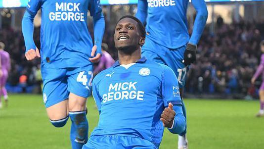 Pemi Aderoju, wearing the blue home shirt of Peterborough United, celebrates scoring against Wigan Athletic