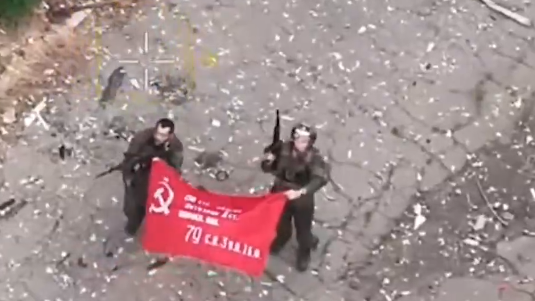 Two men hold a red flag with a hammer and sickle showing they are part of a Russian unit in a video posted by Russia's defence ministry