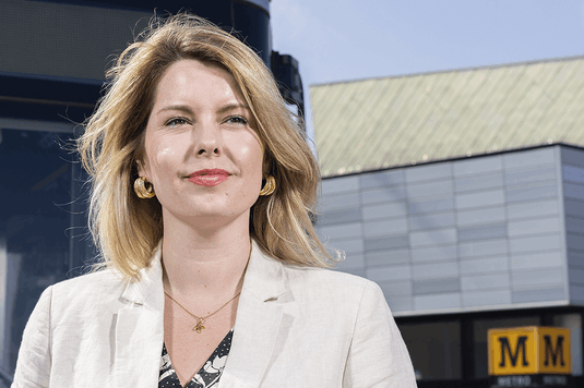 The North East Mayor Kim McGuinness. She has shoulder length blonde hair and is wearing large gold earrings and a cream coloured suit. She is standing outside a Tyne and Wear Metro station. 