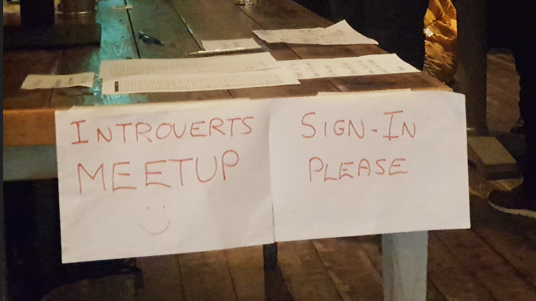 Paper signs taped to a table which say 'introverts meet up' and 'sign-in please' in red ink.