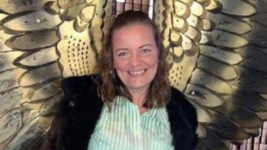 Dianne Cleary is smiling and stood in front of some wall-mounted gold wings to make it look as if they are coming from her back