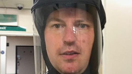 A man in a protective mask looks at the camera