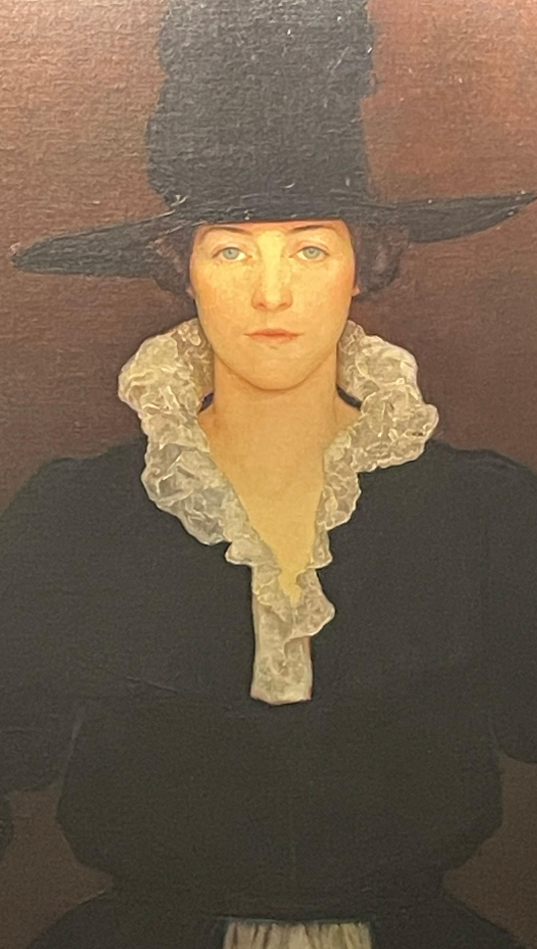 An oil painting of Dorothy dressed in a black dress with a large lace, white collar. The paint is reminiscent of Pilgrim dress and features a large talk black hat. She stares sternly out from the portrait.