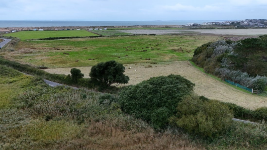 Rugged green fields, with the coast and the sea in the distance.