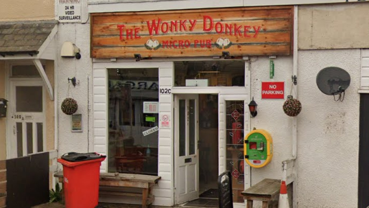 A micropub with a brown sign above the door which reads Wonky Donkey, micro pub. The pub has a white front door and a large window to the left hand side.