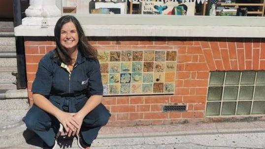 Artist Jayne Wright squatting next to a display of Thanet Tiles of Joy on a wall in a street in Cliftonville 