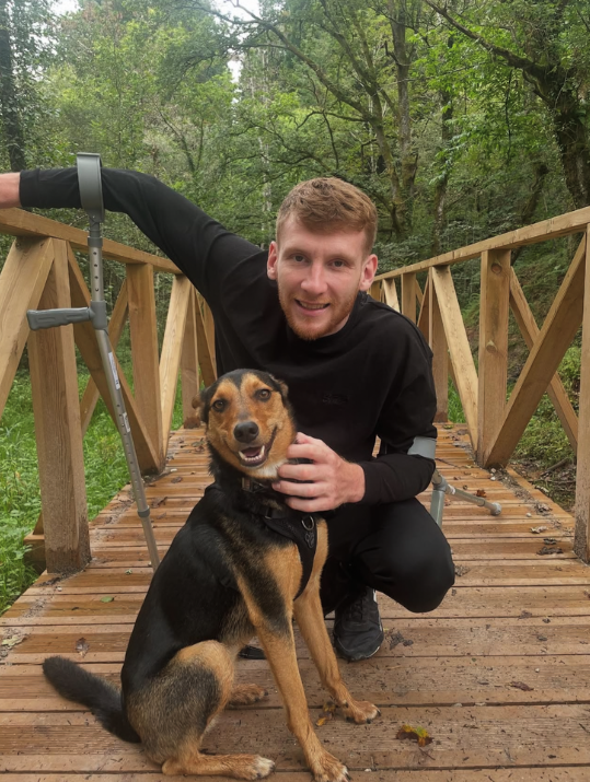 Ben crouching down with his dog on a wooden bridge in the middle of a forest