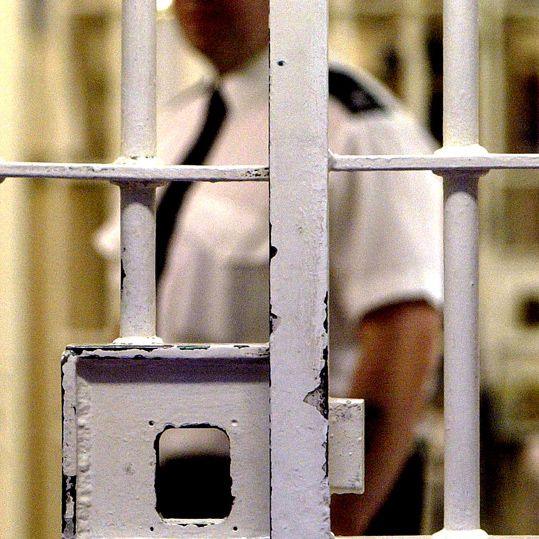 A prison officer is seen behind a barred security door