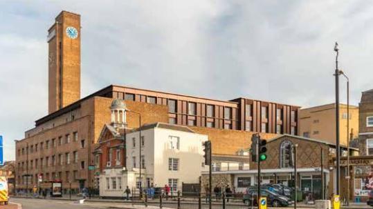 A computer generated image of red brick building with a tall clock tower with a new structure built inside the 1930s original.