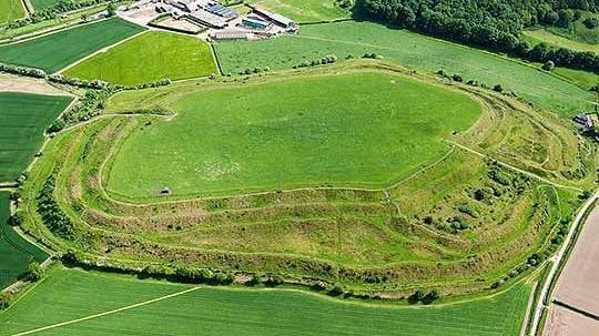 Old Oswestry, an Iron Age hillfort north of Oswestry, a raised area with ramparts, banks and ditches around it in the Shropshire countryside under a blue sky.