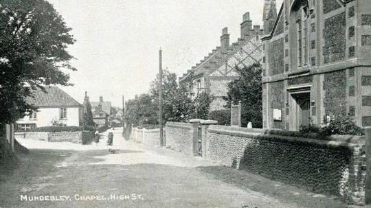 The front of the postcard shows the chapel on the high street in Mundesley. It is a black and white photograph.