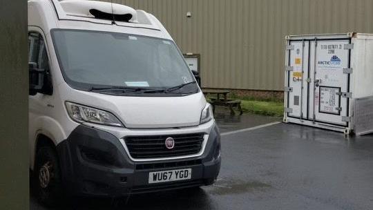 The front of a white refrigerated van, parked on a business park.