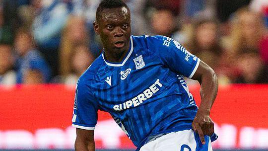 Timothy Ouma playing in blue Lech Poznan shirt with crowd in background.