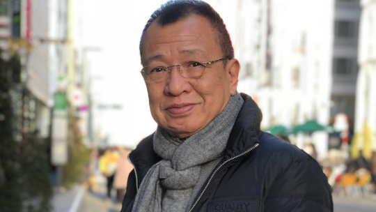 Benz Hui, wearing a scarf and a black jacket, smiles in the photo